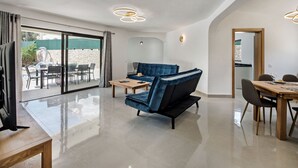A modern living room with a blue sofa, a wooden coffee table, and a dining area with a wooden table and chairs.