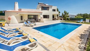 A modern villa with a swimming pool, outdoor seating, and a stone wall.
