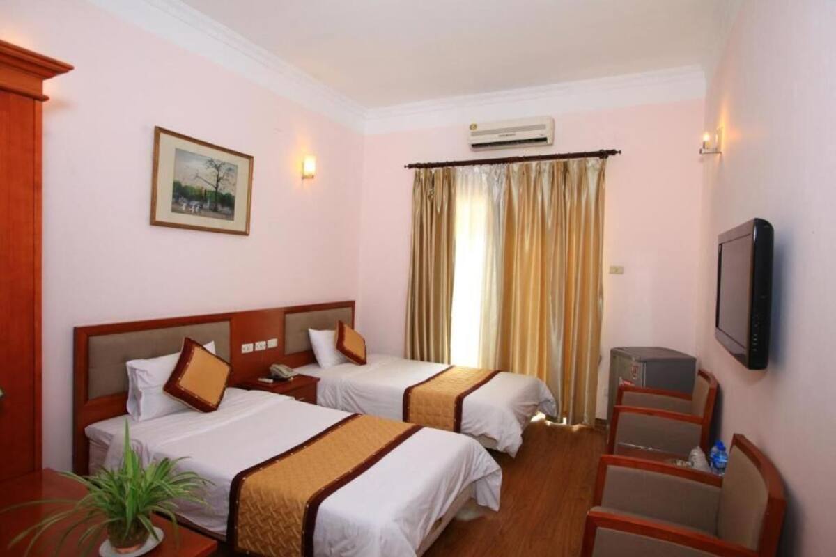 A hotel room with two beds, a TV, a desk, and a potted plant.
