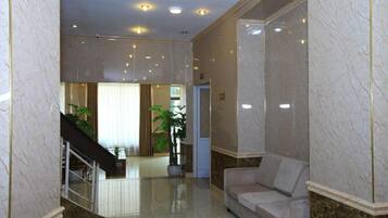 A lobby with marble walls, a staircase, a reception desk, and a sofa.