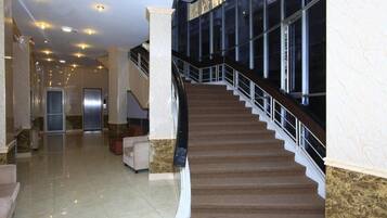 A spacious lobby with a marble floor, a staircase with a handrail, and a view of the building's exterior through large windows.