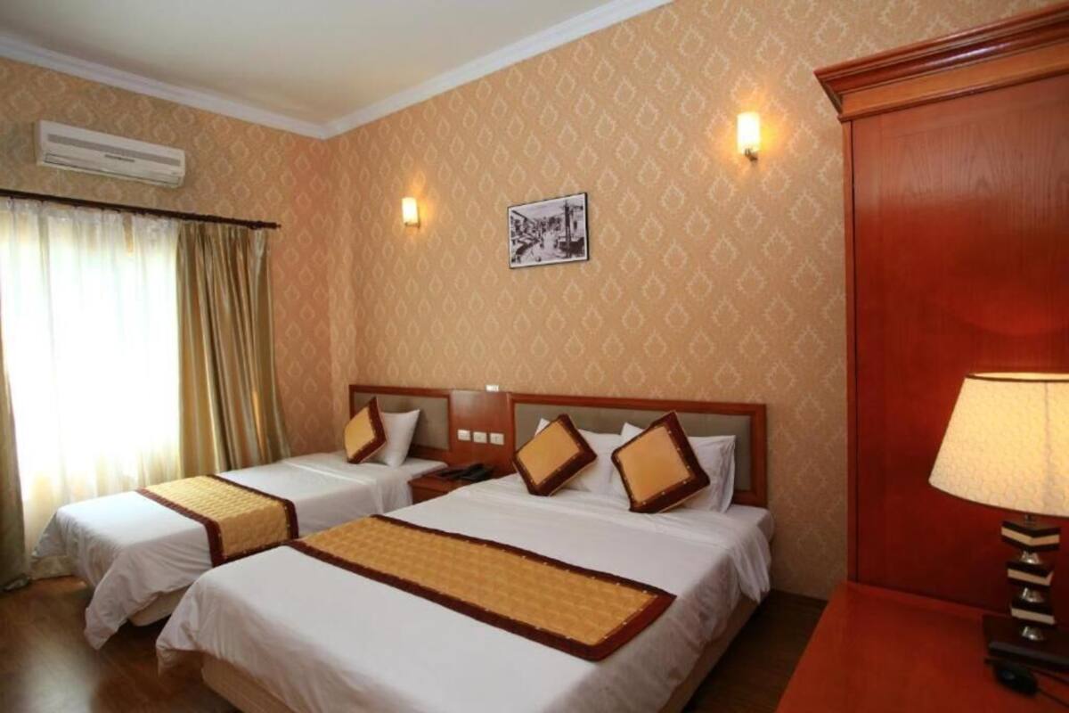 A hotel room with two beds, a nightstand, a lamp, and an air conditioning unit.