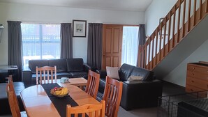 En stue med sofa, spisebord, stole og en trappe.