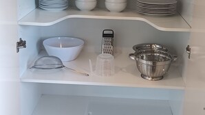 Et spiskab med hylder fyldt med glas, tallerkener, skåle og køkkenredskaber.