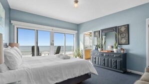 A bedroom with a large bed, a dresser, and a view of the ocean through a sliding door. - Beachfront Rio Del Mar Home - 5 bedrooms! (Aptos)