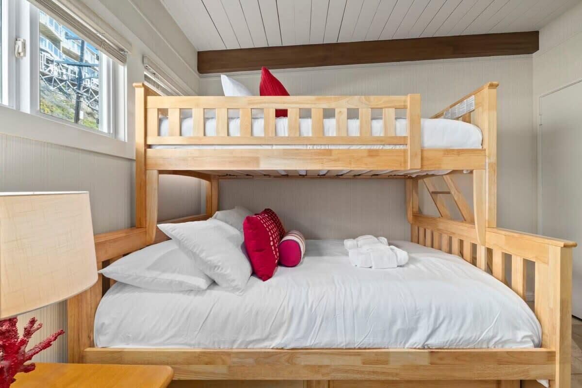 Una cama litera con ropa de cama blanca y almohadas rojas, un cabecero de madera y una lámpara en una mesita de noche.