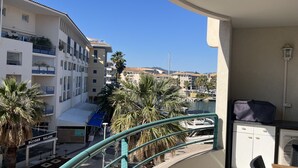 A balcony with a view of a marina, palm trees, and multi-story buildings. - Port-Fréjus, Cesaree Borghèse, 2/3 rooms 52m2, 4 beds, swimming pool, air-conditioned, parking, close access to the beach, large balcony for a pleasant stay in the sun, relaxation and leisure (Fréjus)