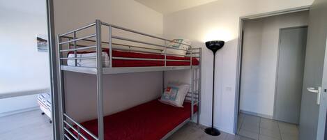 Habitación con literas, un colchón rojo, una lámpara de pie y una puerta.