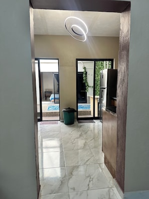 A hallway with a marble floor, a ceiling light fixture, and a view of an outdoor area with a pool and a refrigerator. - Casa a tan Solo 5 Minutos de la Plaza Principal! Ideal Para Familia y Amigos (Tequila)