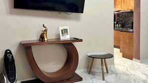A modern living area with a large flat-screen TV mounted on the wall, a wooden console table with a brass faucet, a small round table, and a kitchen visible through an open doorway. - Casa a tan Solo 5 Minutos de la Plaza Principal! Ideal Para Familia y Amigos (Tequila)