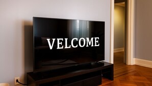 A modern living room with a large flat-screen TV mounted on a wooden stand, a sofa, and a hallway leading to another room. - Family-Friendly 4BR 10min MetLife & American Dream Mall• 20min NYC •Free Parking (North Bergen)