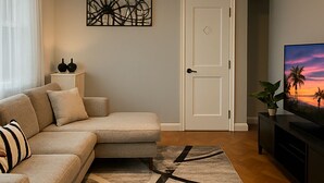 A living room with a sectional sofa, a ceiling fan, a door, and a TV on a stand. - Family-Friendly 4BR 10min MetLife & American Dream Mall• 20min NYC •Free Parking (North Bergen)