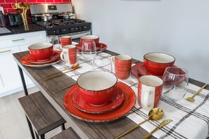 Une cuisine avec une table sur laquelle est disposée une vaisselle rouge et blanche, une cuisinière à gaz et une machine à café.
