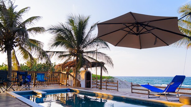 A pool area with lounge chairs and an umbrella, surrounded by palm trees and a wooden deck.