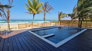A wooden deck with a hot tub, palm trees, and a beach view.