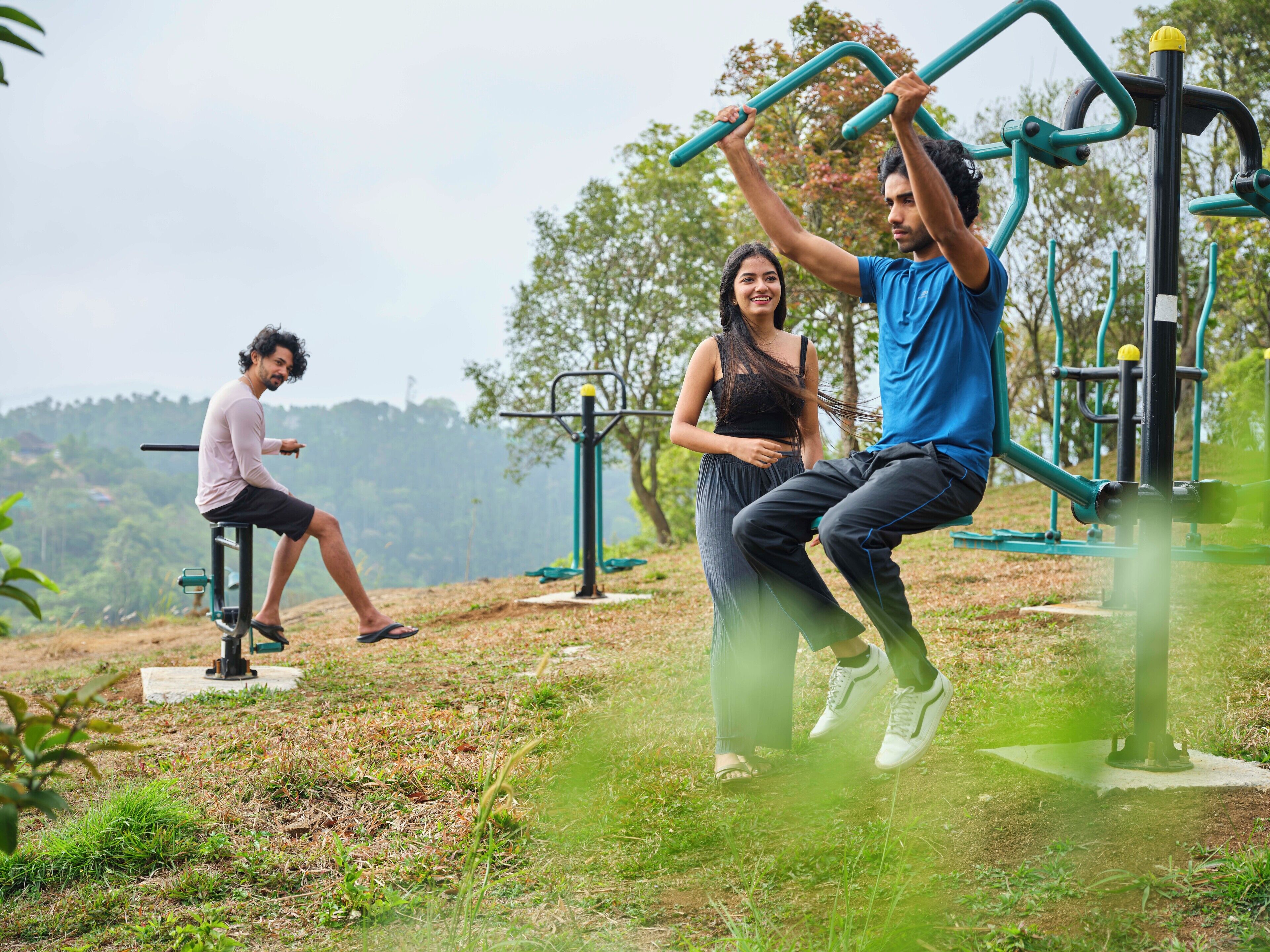 Zona de ejercicios al aire libre con equipamiento de fitness, incluyendo una barra de dominadas y una máquina de prensa de piernas.