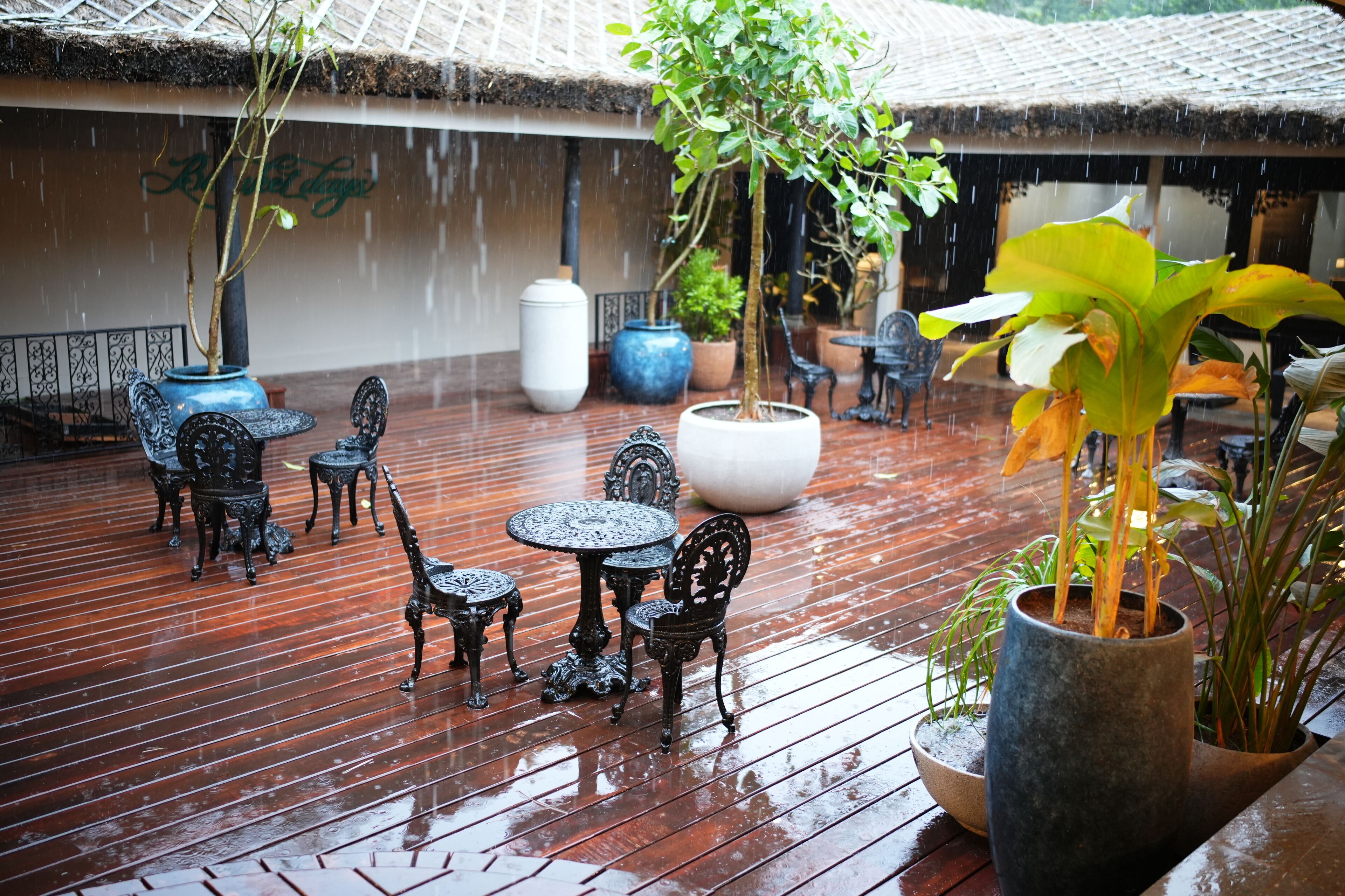 An outdoor patio with wooden flooring, metal tables and chairs, and potted plants.