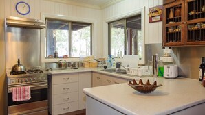 Una cocina con gabinetes blancos, una estufa de acero inoxidable, un fregadero y una ventana con vistas a árboles.