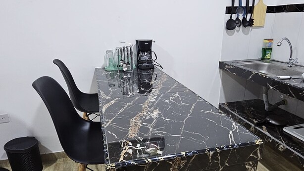 A kitchen with a marble countertop, black chairs, a coffee maker, and a sink.