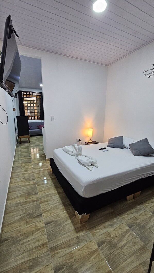 A hotel room with a bed, a bedside lamp, and a TV on a stand.