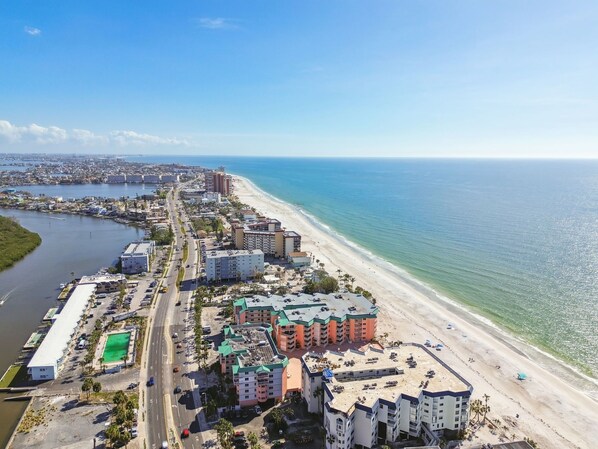 Vista aérea de una ciudad costera con un hotel frente a la playa, un puerto deportivo y una carretera que bordea la playa.