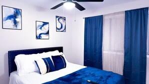 Ein Schlafzimmer mit einem Bett, einem Deckenventilator und drei abstrakten Bildern an der Wand.
