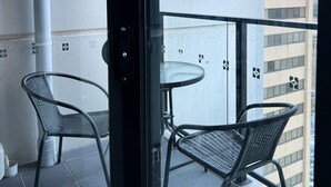 A balcony with two wicker chairs and a small round table, a white tiled floor, and a view of buildings through a glass door. - entire 2 Br apartment city central (Adelaide)