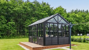 A glass-paneled structure with a wooden deck, surrounded by lush greenery.