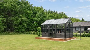 A glass conservatory with a wooden deck, surrounded by a grassy field and trees.