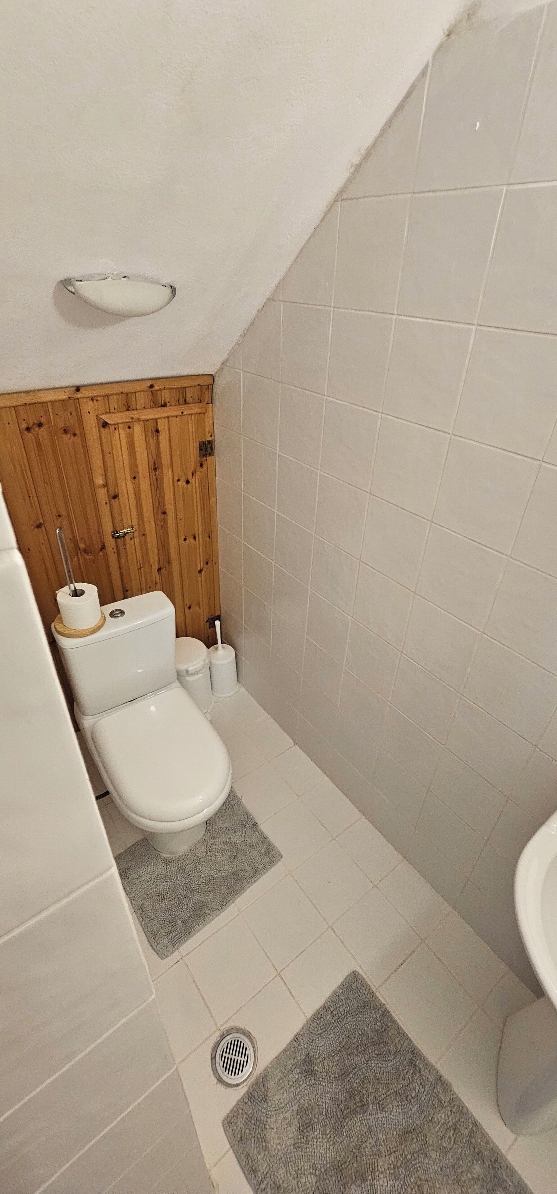 Un bagno piccolo e funzionale con WC, bidet e lavabo. Le pareti sono rivestite di piastrelle e sopra il WC c’è un pannello in legno.