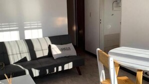 En moderne stue med sofa, et lille bord og en stol. Der er en dør til et badeværelse.