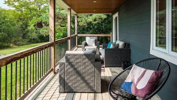 Una terraza cubierta al aire libre con baranda de madera, una zona de estar con sofá y sillones, y vistas a un paisaje verde.