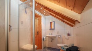 A bathroom with a shower, toilet, sink, and wooden bench. - Ferienwohnung »stadtblick« 50m², 2 Personen, Nichtraucher, Balkon, W-lan (Traunstein)