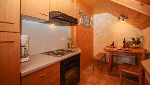 A compact kitchen with wooden cabinets, a stove, and a dining area with a table and chairs. - Ferienwohnung »stadtblick« 50m², 2 Personen, Nichtraucher, Balkon, W-lan (Traunstein)