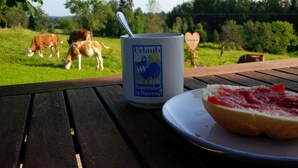 A table with a can and a plate of food, a wooden bench, and a view of cows grazing in a field. - Ferienwohnung »stadtblick« 50m², 2 Personen, Nichtraucher, Balkon, W-lan (Traunstein)