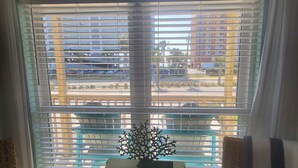 A room with a view of a parking lot and buildings, a sign reading "BEACH HOUSE", a small table with a decorative coral piece, and two wicker chairs.