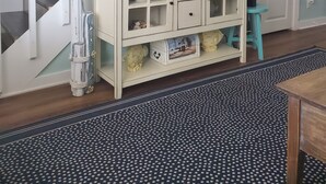 A room with a staircase, a television on a cabinet, a small stool, and a patterned rug.