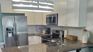 A modern kitchen with a stainless steel refrigerator, a microwave, a stove, and a sink. There are four bar stools and a wooden island with a built-in sink.