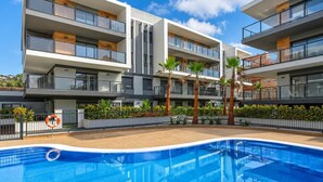 A modern multi-story building with a swimming pool, balconies, and tropical plants.