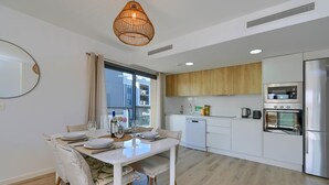 A modern kitchen with white cabinets, a stainless steel refrigerator, and a dining area with a white table and chairs.