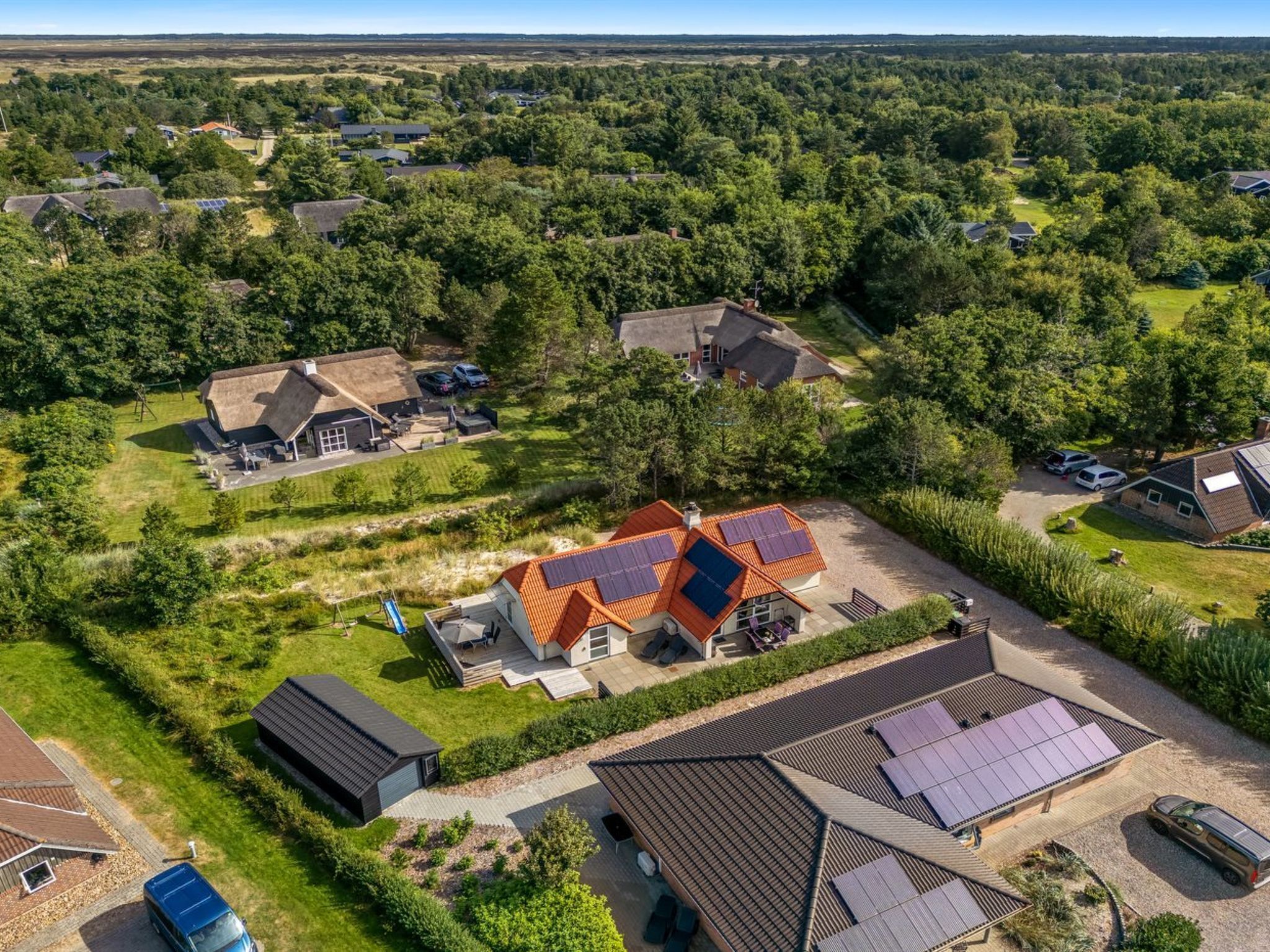 Zona residencial con varias casas, algunas con paneles solares, rodeada de vegetación.