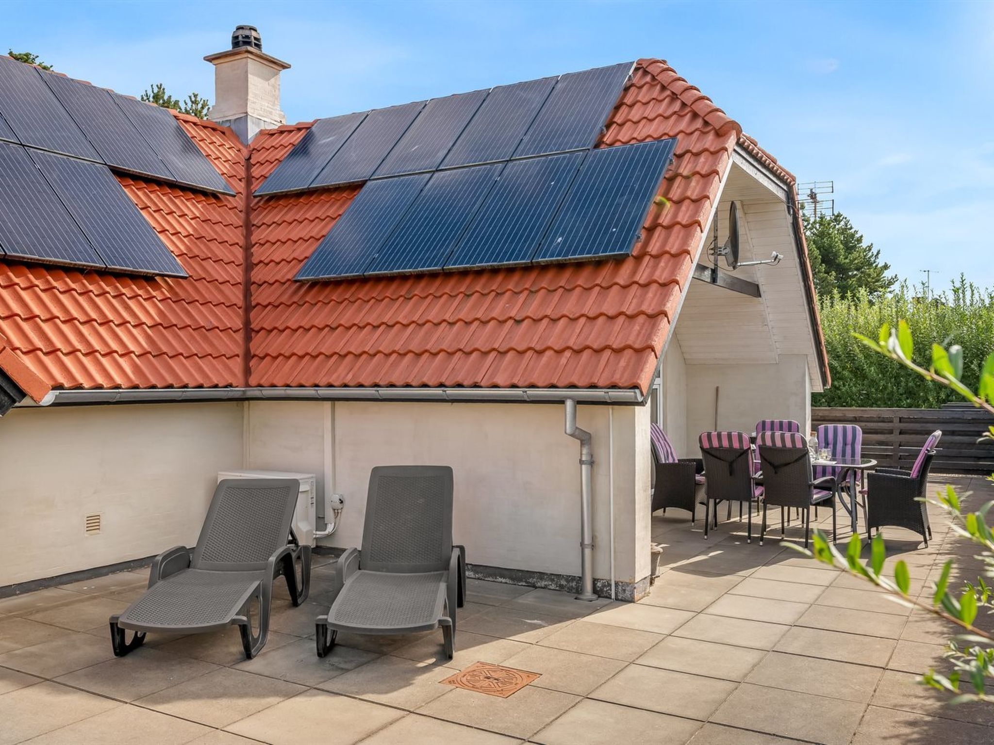 A house with a sloped red roof, solar panels, and a patio with chairs and a table.