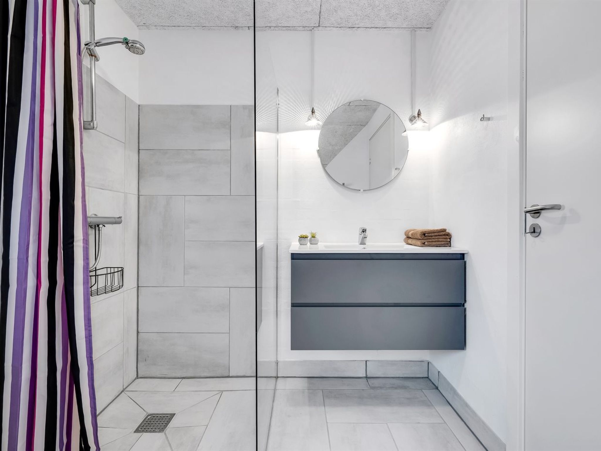 Une salle de bain moderne avec une douche à l’italienne, un lavabo avec un miroir au-dessus et un porte-serviettes.