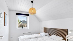 Ein modernes Schlafzimmer mit zwei Betten, einer geneigten Decke, einem großen Fenster und Blick auf ein Haus.