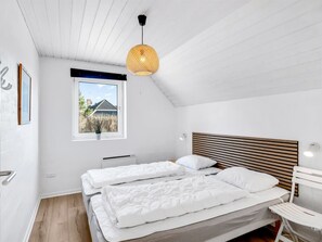 Une chambre moderne avec deux lits, un plafond en pente, une grande fenêtre et une vue sur une maison.