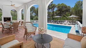 Un espacio al aire libre cubierto con piscina, mobiliario de mimbre y chimenea.
