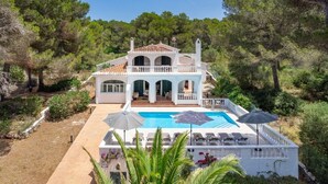 Una casa de dos pisos con piscina, rodeada de árboles y vegetación.
