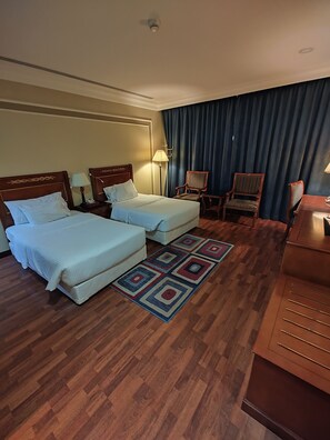 A hotel room with two beds, a desk, a chair, a lamp, and a patterned rug. - Karim Hotel Al Olya (Al Khobar)