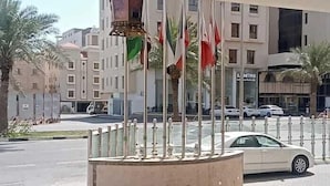 A hotel entrance with a decorative lantern, multiple flags, and a view of the street with cars and buildings. - Karim Hotel Al Olya (Al Khobar)