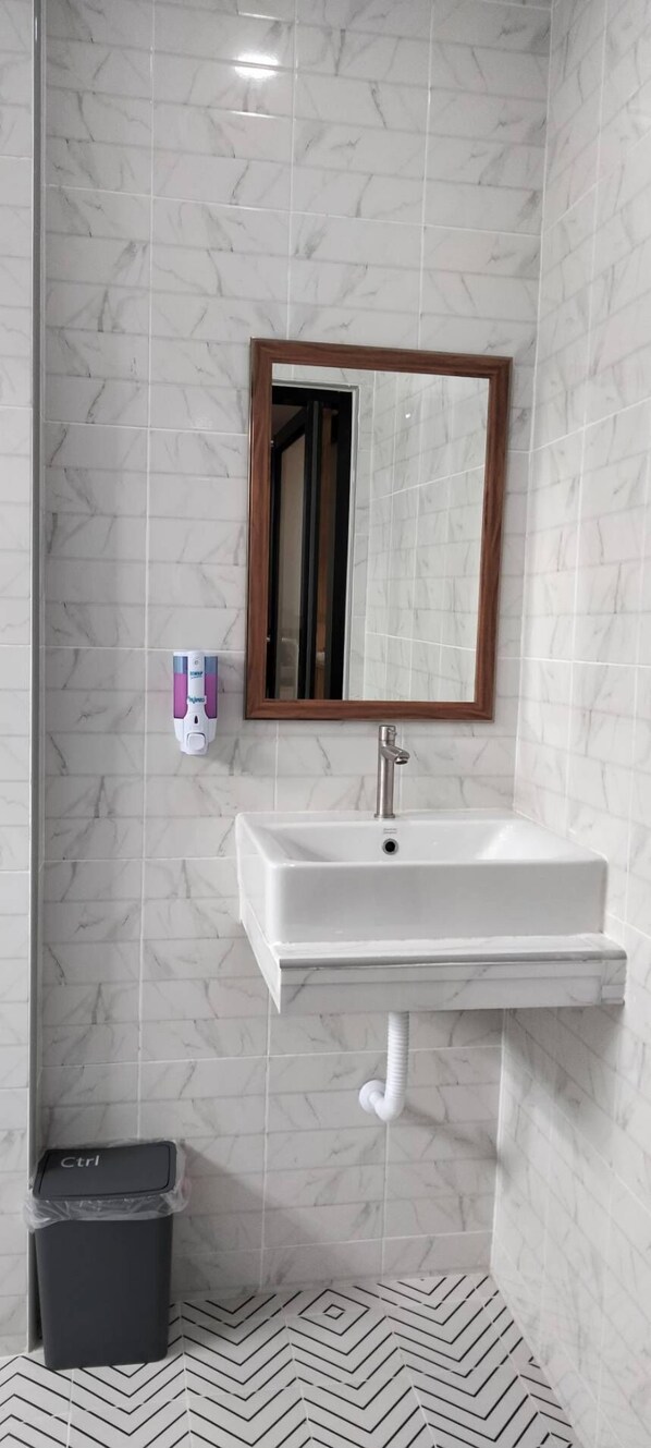 Un baño con un lavamanos blanco, un espejo con marco de madera y un dispensador de jabón.